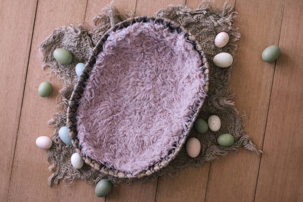 Pasgeboren digitale achtergrond - ovale geweven schaal met roze nepbont, jutelaag en paaseieren op houten ondergrond. Pasgeboren Pasen achtergrond textuur - Foto, afbeelding