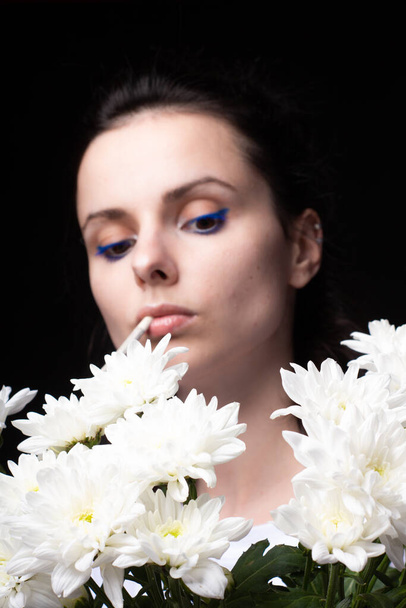 woman with a bouquet of white flowers smokes a cigarette, black studio background - Foto, immagini