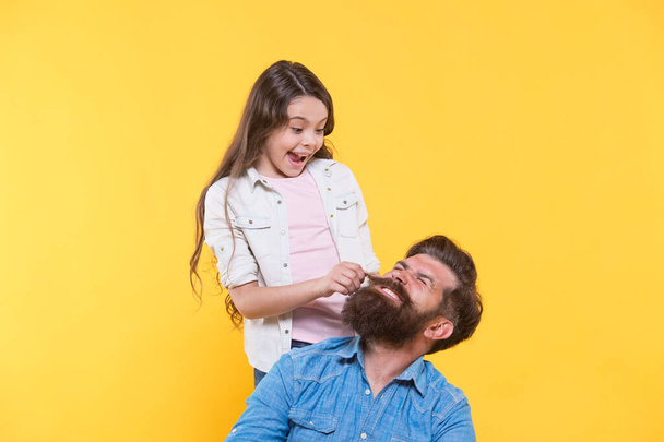 My father is hipster. Little girl pull hipster beard. Happy family yellow background. Hipster barbershop. Barber shop. Hair salon. The bushy beard is great - Foto, Imagen