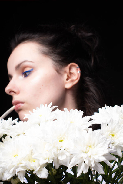 woman with a bouquet of white chrysanthemums smokes a cigarette, dark studio background - Photo, Image