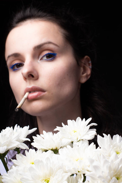 woman with a bouquet of white chrysanthemums smokes a cigarette, dark studio background - Foto, Imagem