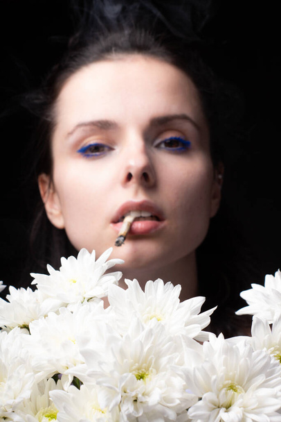 woman with a bouquet of white chrysanthemums smokes a cigarette - 写真・画像