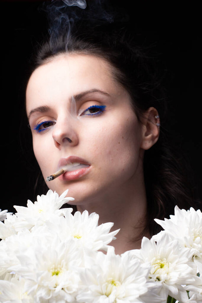 woman with a bouquet of white chrysanthemums smokes a cigarette - Photo, Image