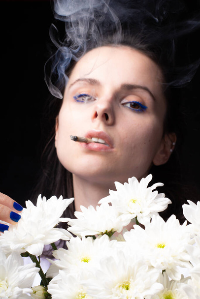 woman with a bouquet of white chrysanthemums smokes a cigarette - Фото, изображение