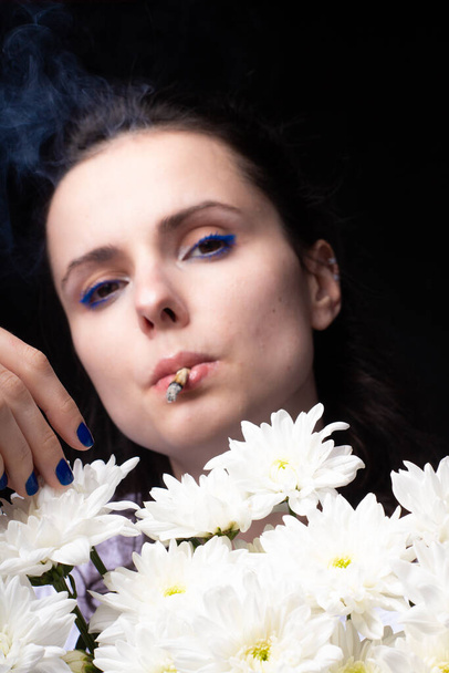 woman with a bouquet of white flowers smokes a cigarette - Zdjęcie, obraz