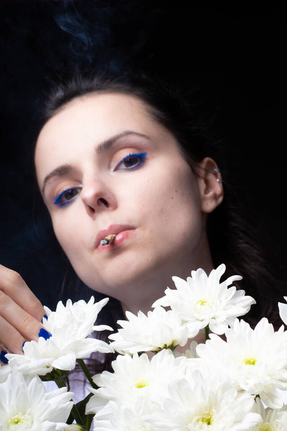 woman with a bouquet of white flowers smokes a cigarette - Valokuva, kuva