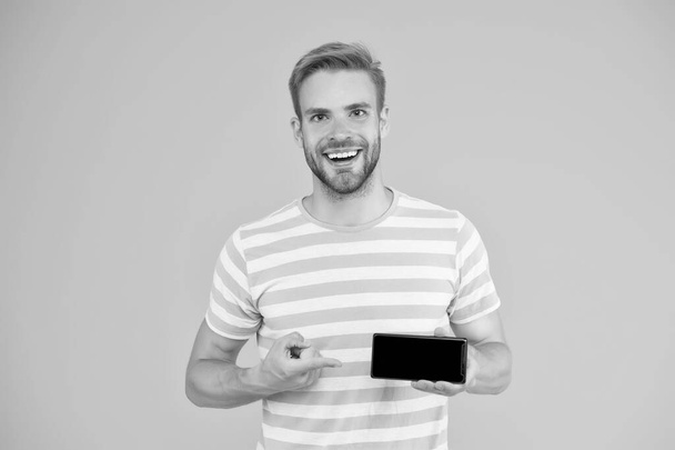 Best phone available for you. Happy guy pointing at smartphone yellow background. Pointing for advertising. Index finger pointing. Pointing gesture. Top pick. It will actually make your life easier - Fotografie, Obrázek