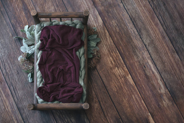 Newborn thanksgiving  digital background - dark wooden bed with sage green knitted blanket and maroon layer and sage plant branches and leaves on dark wooden background - Photo, Image