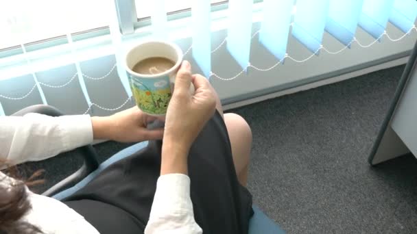 Woman sitting by the office windows with a cup of coffee - Záběry, video