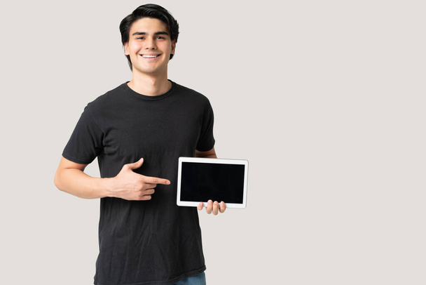 笑顔ヒスパニック系の若い男を保持デジタルタブレットとその空白の画面を示す - 写真・画像