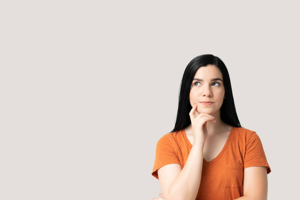 Mujer joven reflexiva mirando hacia arriba mientras está de pie con la mano en la barbilla - Foto, Imagen