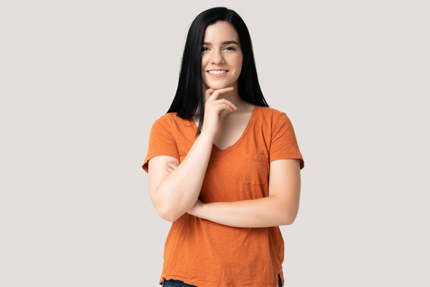 Lächelnde junge Frau im orangefarbenen T-Shirt mit der Hand am Kinn - Foto, Bild