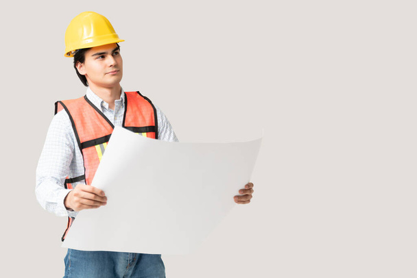 Zamyšlený mladý muž stavební inženýr v reflexní vestě a hardhat drží stavební plán - Fotografie, Obrázek
