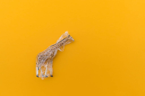La jirafa está enredada en una bolsa de plástico. Concepto plástico animal. Fondo amarillo. Problema de contaminación ambiental
. - Foto, imagen
