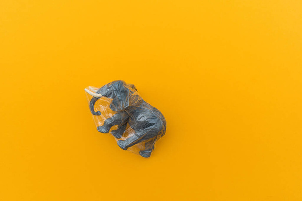 Elephant is entangled in a plastic bag. Plastic animal concept. Yellow background. Environmental pollution problem. - Fotó, kép