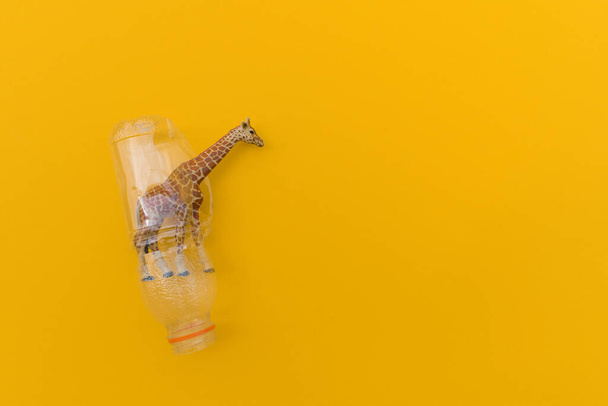 Giraffe is entangled in a plastic bag. Plastic animal concept. Yellow background. Environmental pollution problem. - Foto, imagen