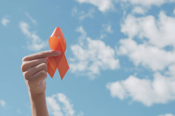 Hands holding orange Ribbon over blue sky,  Leukemia cancer and Multiple sclerosis, COPD and ADHD awareness, world kidney day - Fotografie, Obrázek