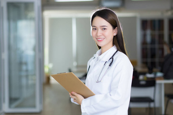 Asian woman doctor is smiling and standing confidently while she holds the document clipboard in her hands. - Photo, Image