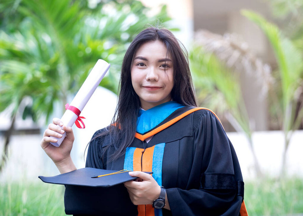 Portrét šťastné a vzrušené mladé asijské absolventky vysoké školy nosí maturitní šaty a klobouk slaví s titulem v univerzitním kampusu na začátku dne. Vzdělávací stock fotografie. - Fotografie, Obrázek