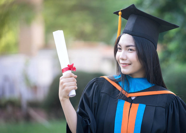 Πορτρέτο της ευτυχισμένος και ενθουσιασμένος της νεαρής ασιάτισσας απόφοιτος πανεπιστημίου φοράει φόρεμα αποφοίτησης και καπέλο γιορτάζει με πτυχίο στην πανεπιστημιούπολη κατά την ημέρα έναρξης. Εκπαίδευση φωτογραφία αρχείου. - Φωτογραφία, εικόνα