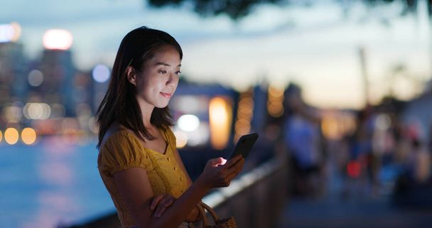 Γυναίκα χρήση του κινητού πάνω από την πόλη νυχτερινή θέα - Φωτογραφία, εικόνα