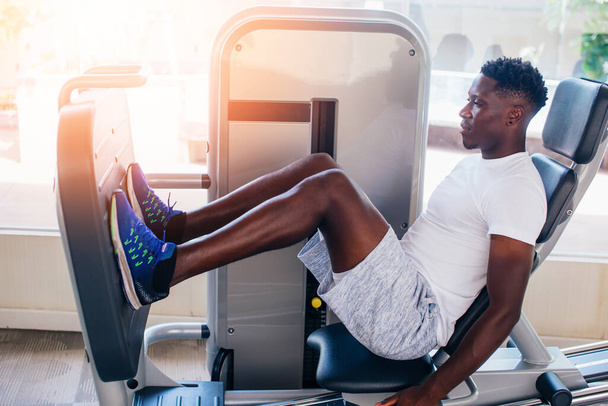 Back view of African American man doing exercise on leg press during fitness training in modern gym - Fotó, kép