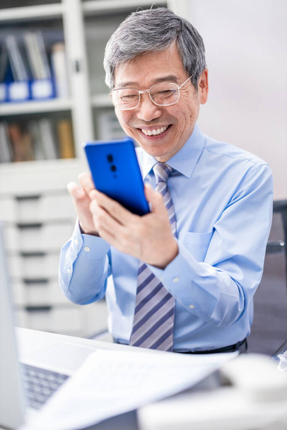 asian elder businessman use smartphone happily in the office - Foto, Bild