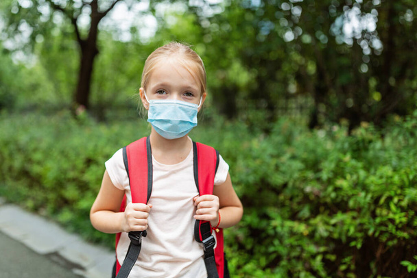 School child wearing face mask during coronavirus pandemic outbreak. Blonde girl going back to school after covid-19 quarantine and lockdown. Kid in medical mask for coronavirus prevention. New normal. High quality photo - Φωτογραφία, εικόνα