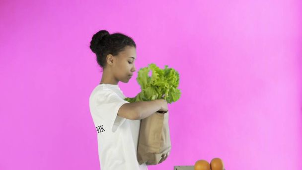 Mujer feliz carga bolsa de papel con verduras orgánicas saludables y frutas sobre fondo rosa
 - Foto, Imagen