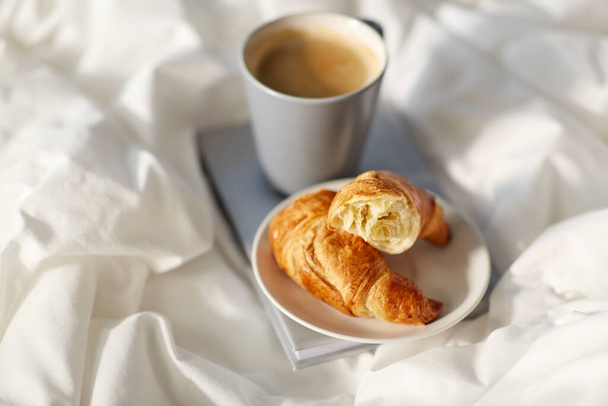 croissants, cup of coffee and book in bed at home - Foto, Bild