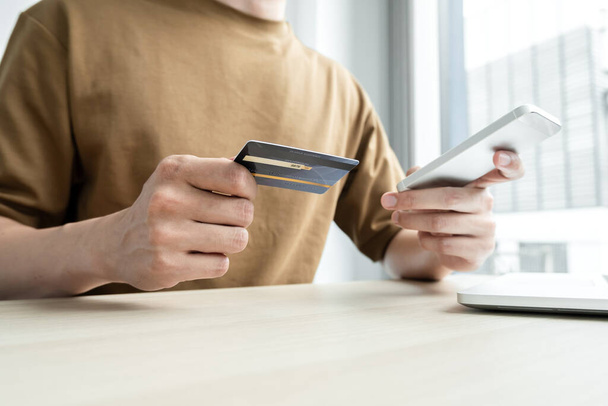 Die Hand des Geschäftsmannes hält eine Kreditkarte und benutzt ein Smartphone für Online-Einkäufe und Internet-Zahlungen im Büro. - Foto, Bild