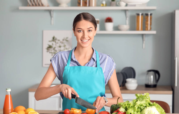 Beautiful young woman making vegetable salad in kitchen - Foto, afbeelding