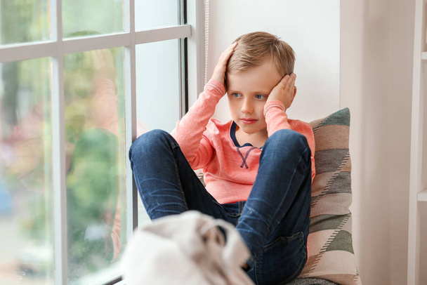 Niño triste con trastorno autista sentado cerca de la ventana en casa
 - Foto, Imagen