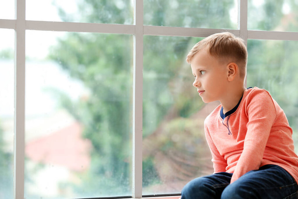 Μικρό αγόρι με αυτιστική διαταραχή κάθεται κοντά στο παράθυρο στο σπίτι - Φωτογραφία, εικόνα