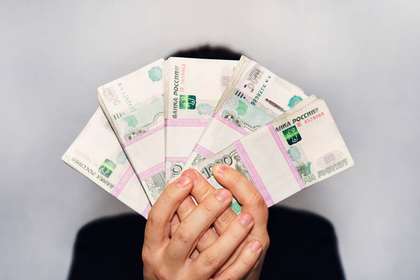 Viel Geld in der Hand eines jungen Geschäftsmannes auf blauem Grund. Ein Stapel russischer Rubel-Banknoten mit einem Nennwert von 1000 Rubel. Erfolgreicher Geschäftsmann - Foto, Bild