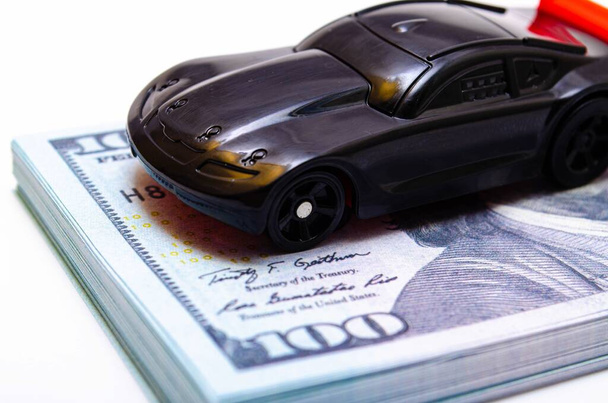 A toy sports car in black with a red wing on a springboard, a podium made of dollar bills. Car and dollars. Buying, selling price increases in the market - Photo, Image