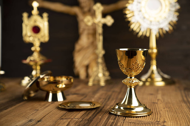 Catholic religion symbols. The Cross, monstrance, Jesus figure, Holy Bible and golden chalice on the rustic wooden altar. - Photo, Image