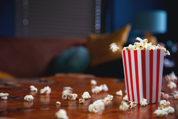 Popcorn flying out of cardboard box. red and white striped popcorn bucket with flying popcorn in the living room, movie or cinema concept - Photo, Image