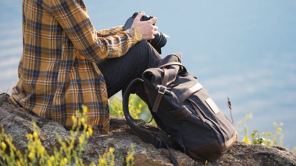 Young adult in shirt with dark gray backpack holding a camera for landscape photography. Travel concept - Fotoğraf, Görsel