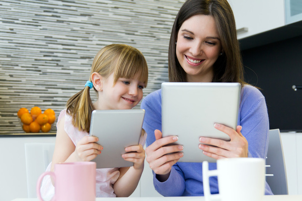 Mother and daughter using a digital tablet in kitchen - Foto, afbeelding