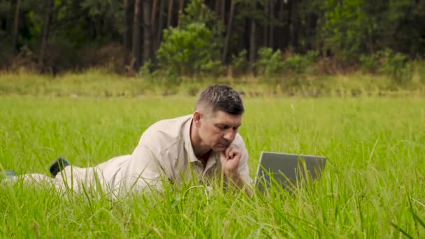 Geschäftsmann arbeitet hinter einem Laptop, der im Gras liegt - Filmmaterial, Video