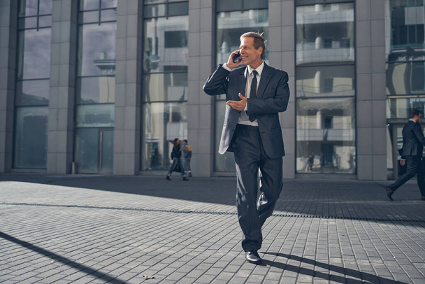 Cheerful businessman having phone conversation on the street - Photo, image