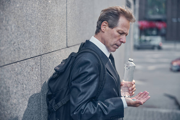 Good-looking man in suit holding pill and bottle of water - Фото, зображення