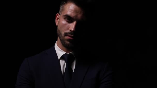 таємничий молодий бізнесмен у костюмі, що стоїть і позує в модному світлі, схрещуючи руки і фіксуючи костюм і краватку на темному фоні
 - Кадри, відео