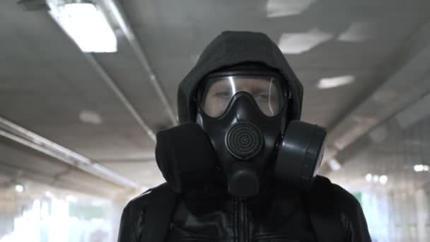 άνδρας με μάσκα αερίου, μαύρο μπουφάν με κουκούλα που περπατάει μέσα από μακρύ τούνελ, υπόγεια διάβαση - Πλάνα, βίντεο