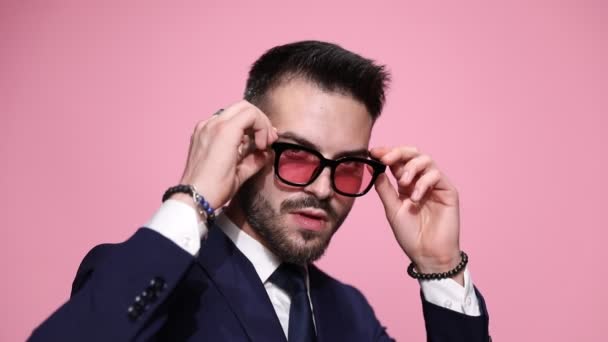 κοντινό πλάνο ενός σέξι σαγηνευτικού επιχειρηματία που βγάζει τα γυαλιά του, κοιτάζει βαθιά μέσα στην κάμερα δείχνοντάς την με τα γυαλιά του, γυρνώντας την πλάτη του και αφήνοντας ροζ φόντο - Πλάνα, βίντεο