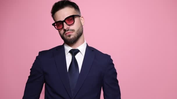 homem de negócios de moda legal posando com estilo contra fundo rosa, vestindo óculos de sol, virando-se e arrumando sua jaqueta, fazendo um sinal de calado, girando e saindo
 - Filmagem, Vídeo