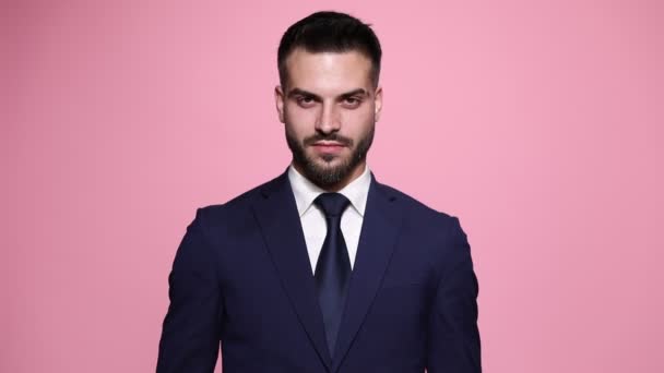 cool businessman with attitude looking at camera, crossing his hands at his chest, smiling and pointing forward on pink background - Footage, Video