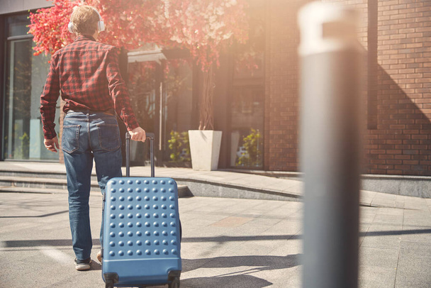 Stylish man carrying travel suitcase on the street - Фото, зображення