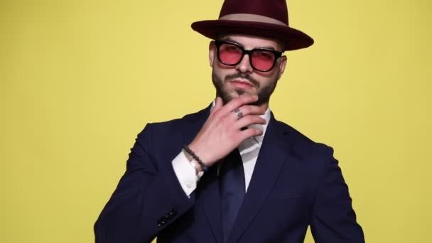 elegante jonge sexy zakenman in pak met zonnebril en hoed, hand in hand en aanraken kin, bewegen in een zijaanzicht positie en lopen weg op gele achtergrond - Video
